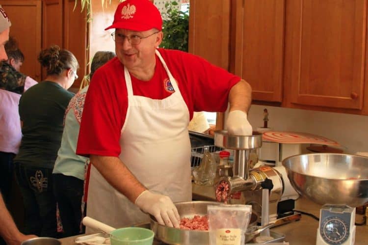 A person cooking in a kitchen preparing food, with Sausage and Kielbasa