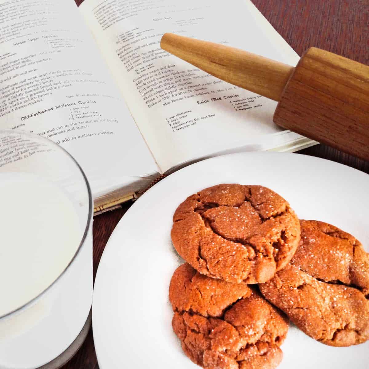 Plate of molasses cookies with a rolling pin, a glas of milk and the Mennonite Community Cookbook.