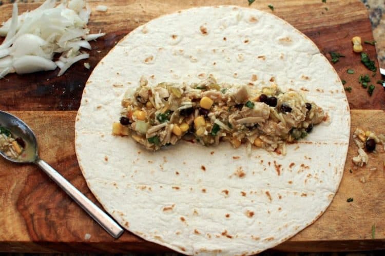 A tortilla wrapper with chicken filling sitting on top of a wooden table