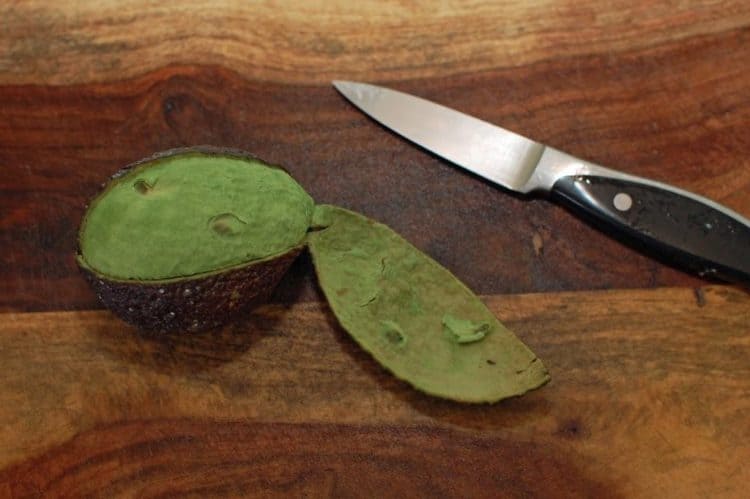 A knife sitting on top of a wooden cutting board, with Avocado