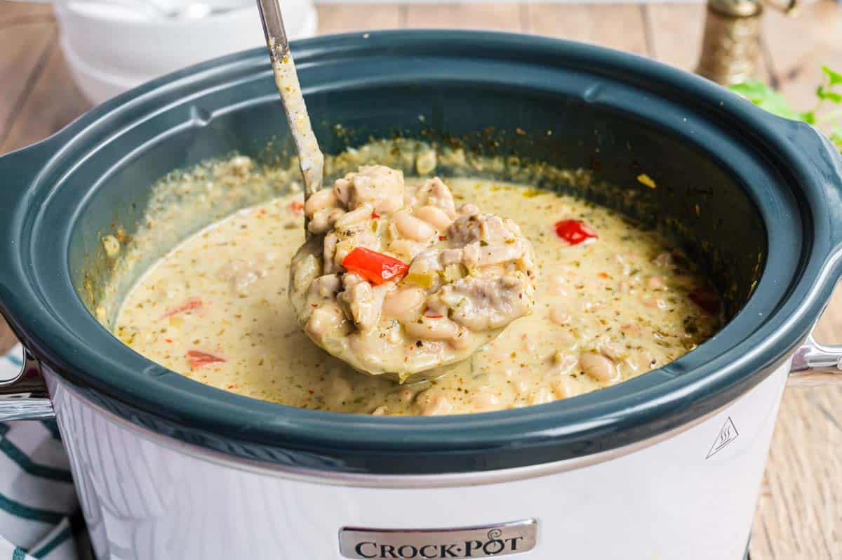 A ladle of white chicken chili from a crock pot.