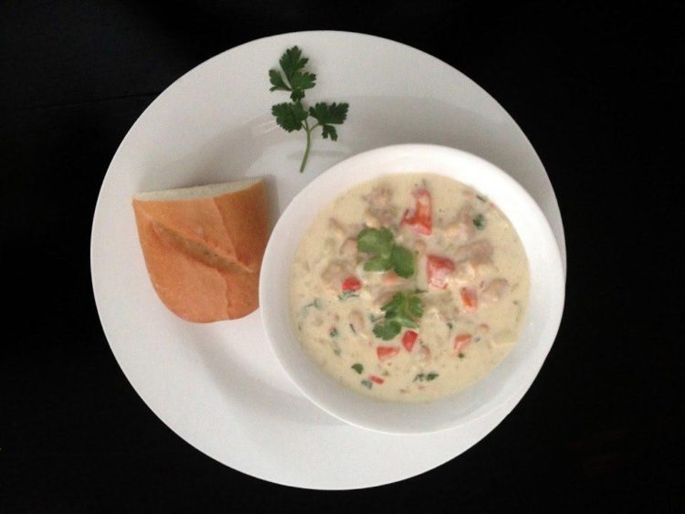 A bowl of chili on a plate with a roll