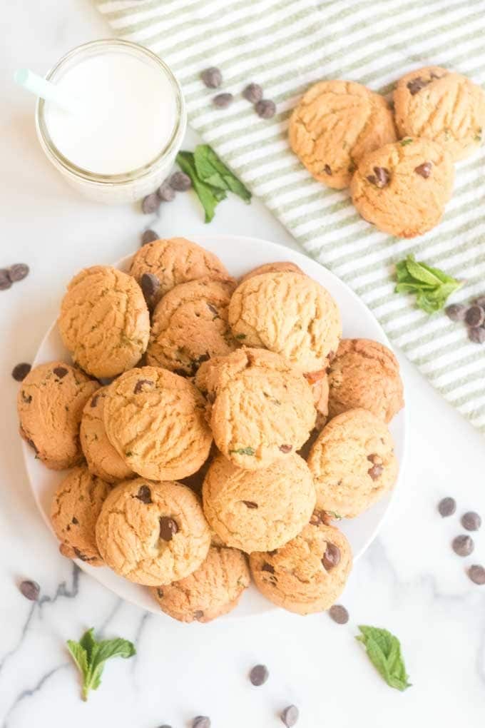 Round plate of mint chocolate chip cookies and fresh mint leaves.