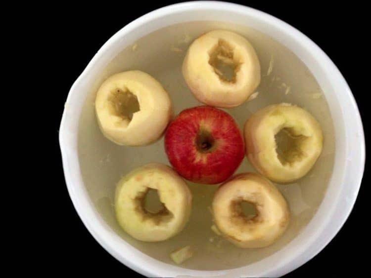 Cored apples sitting in a bowl of water.