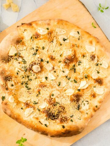 A garlic pizza on a cutting board.