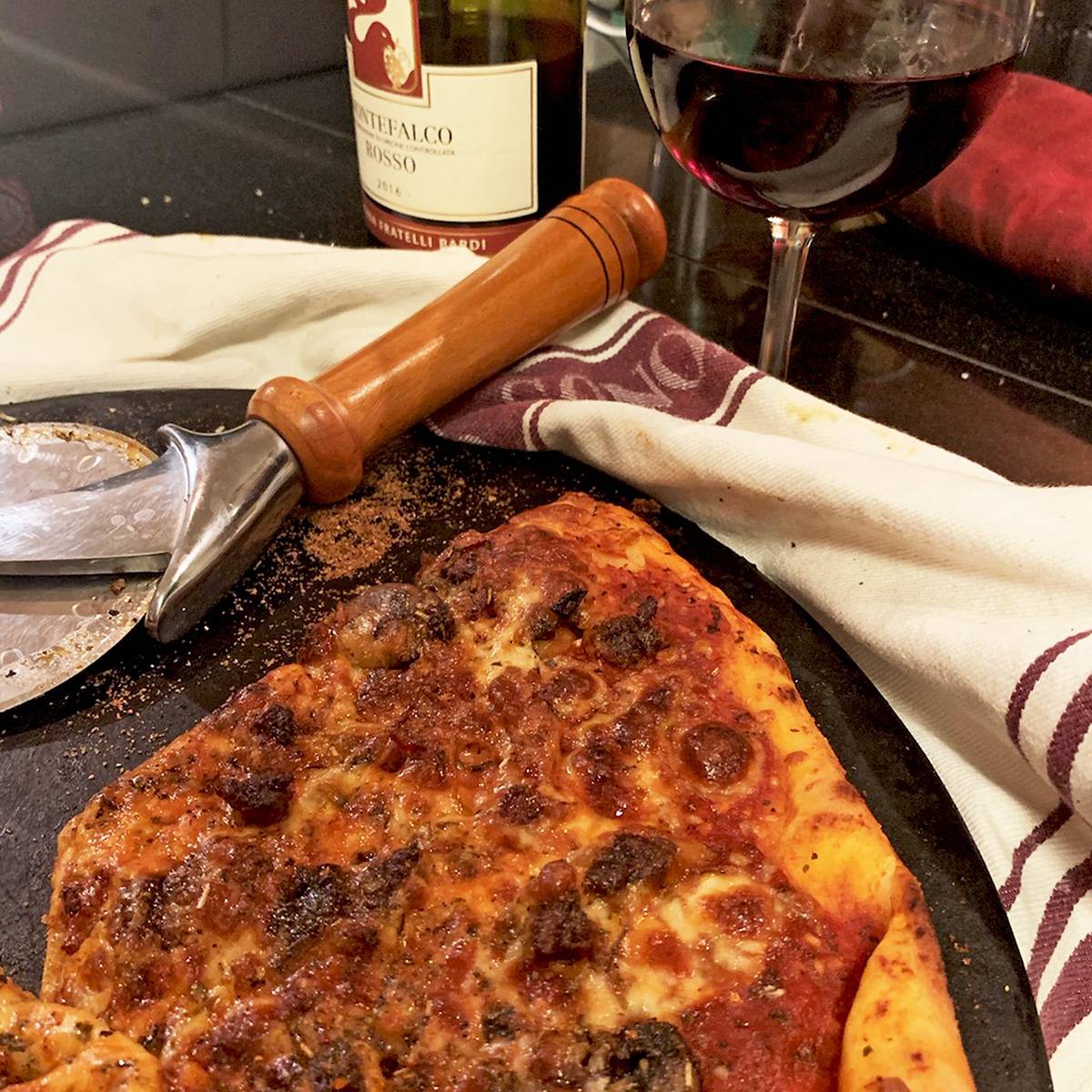 A pizza on a baking stone with a glass of red wine