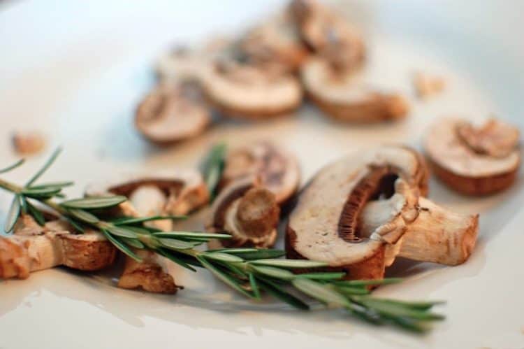 A plate of sliced mushrooms with a rosemary spring