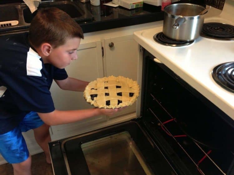 A boy putting a homemade pie in the oven