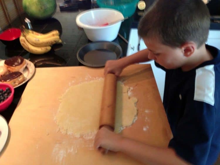 A young boy rolling out a pie crust