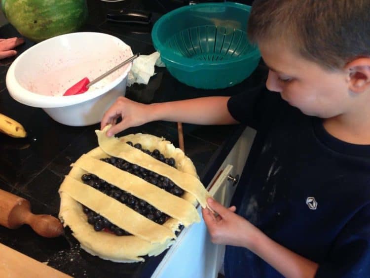 A boy putting a lattice crust on a blueberry pie