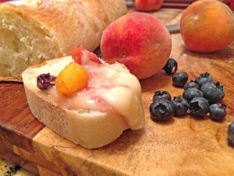 A peach sitting on top of a wooden cutting board, with Peach and Brie