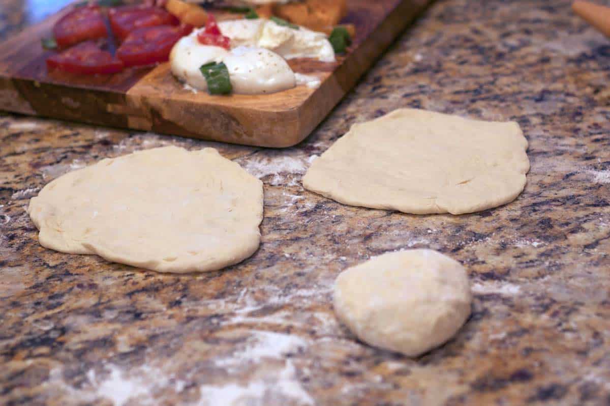 Some pizza dough being flattened on a kitchen counter top.