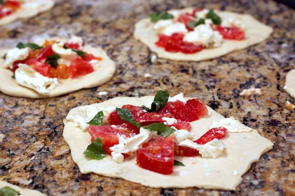 Some portions of pizza dough with burrata cheese and tomatoes on top.