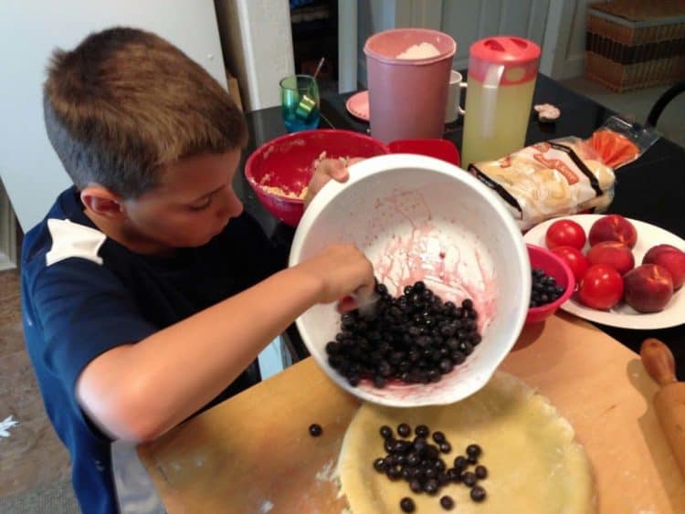 A young boy making a blueberry pie