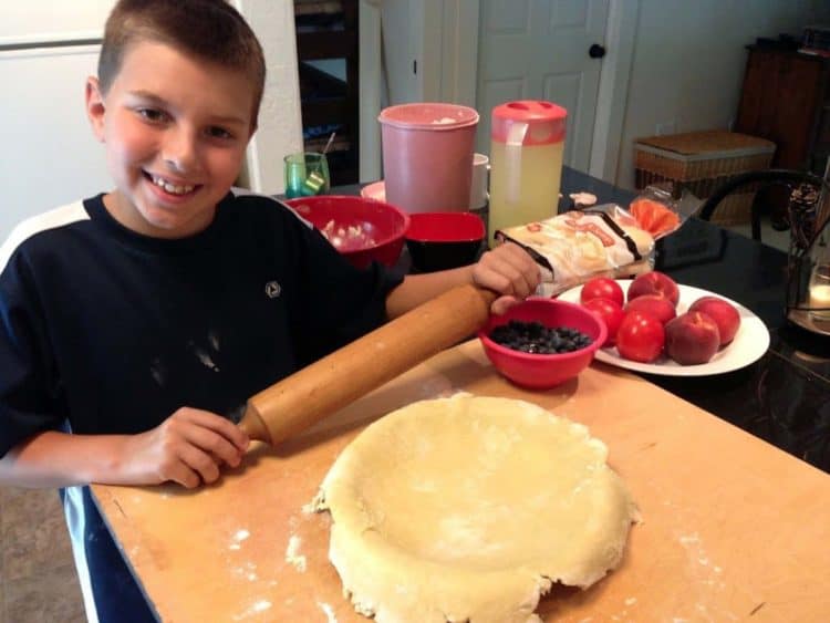 A boy holding a rolling pin over a pie crust