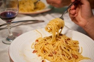 A person holding a fork with carbonara.