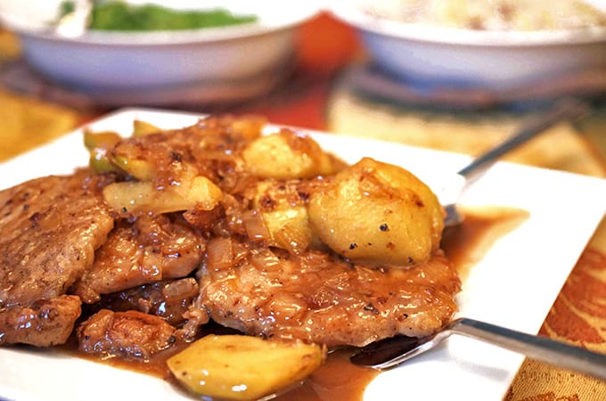 Plated cooked pork and apples in sauce with 2 serving utensils
