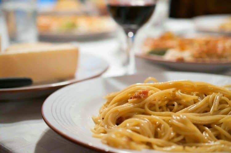 A plate of carbonara with a glass of wine.