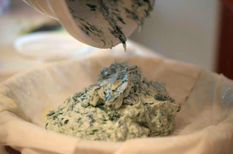A cheese and spinach mixture getting dumped into a pie crust.