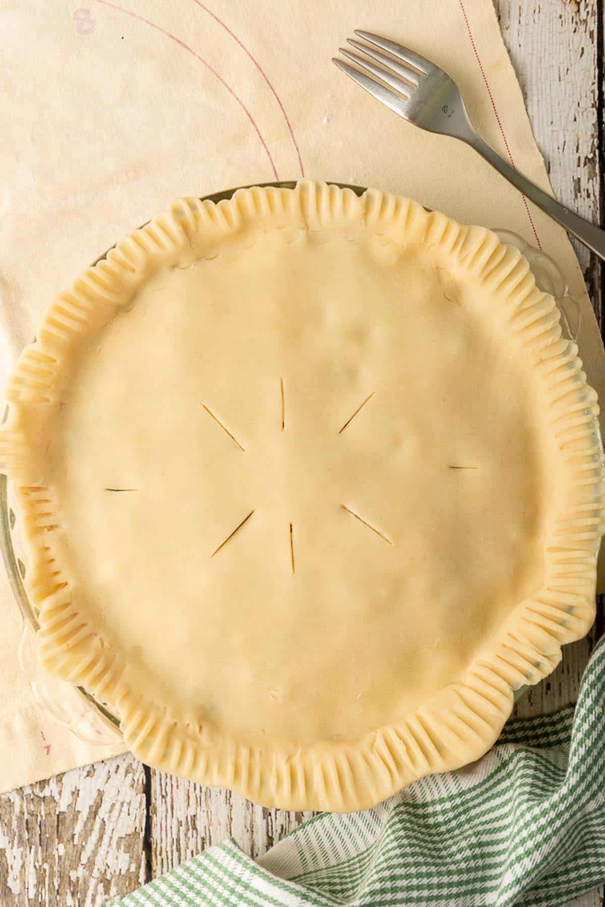 An unbaked chicken pot pie with slits cut into the top crust.