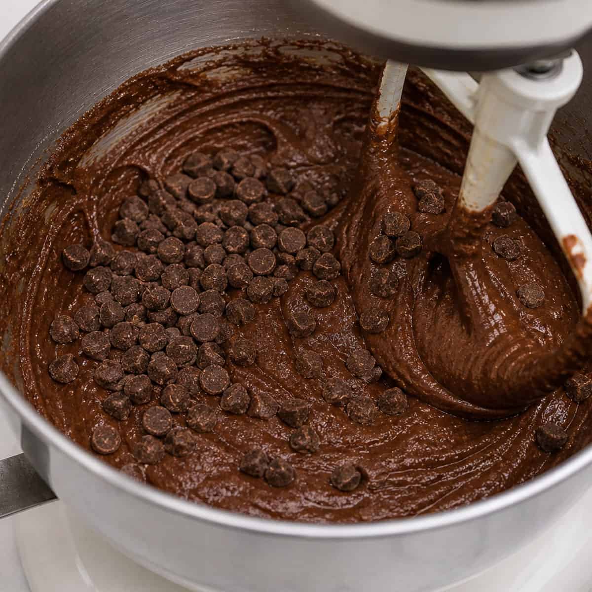 A bowl of brownie batter with chocolate chips being mixed in.
