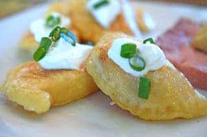 A close up of plated pierogi on plate with sour cream and scallion garnish