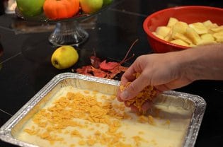 Someone sprinkling ingredients in aluminum pan with cut and whole apples background