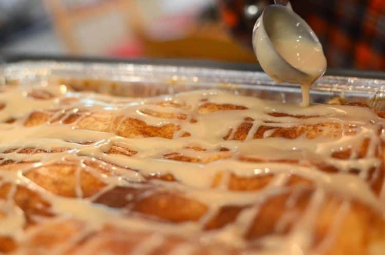 Close up of baked apple dessert bars being drizzled with sugar glaze in cup