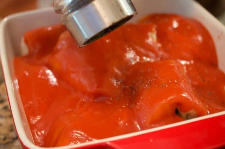 A close up of tomato product in dutch oven, someone adding pepper from above