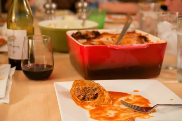 Dinner table halved stuffed cabbage on plate with fork, serving dish with utensil behind  