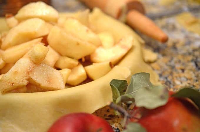 A close up apple pie in preparation with rolling pin and whole apple on counter