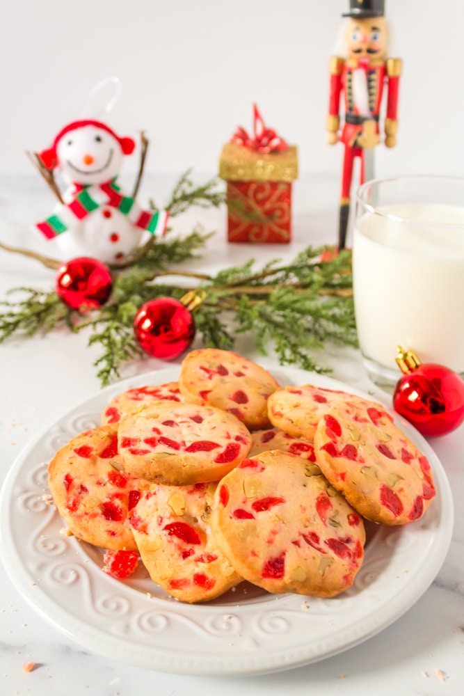 Plate of Cherry Christmas cookies with garland and a glassof milk.