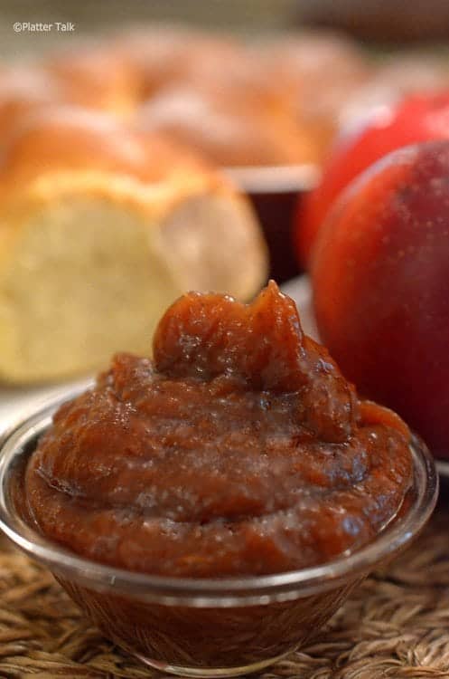 Bowl of homemade apple butter with dinner rolls and an apple in the backgropund.