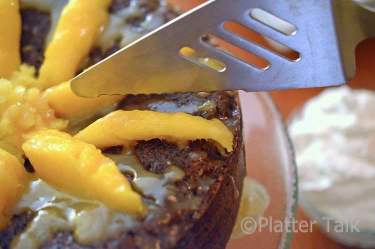 a person about to cut a ginger cake with mango and brandy glaze