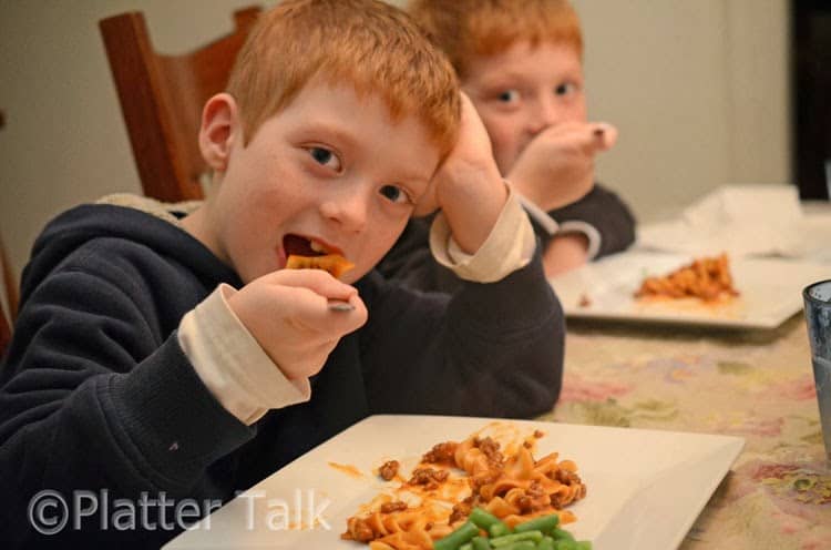 Two little boys sitting at a table eating food