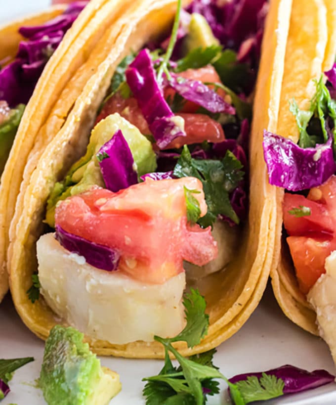 Closeup photo of fish taco, overflowing with tomatoe, avocado and cole slaw.