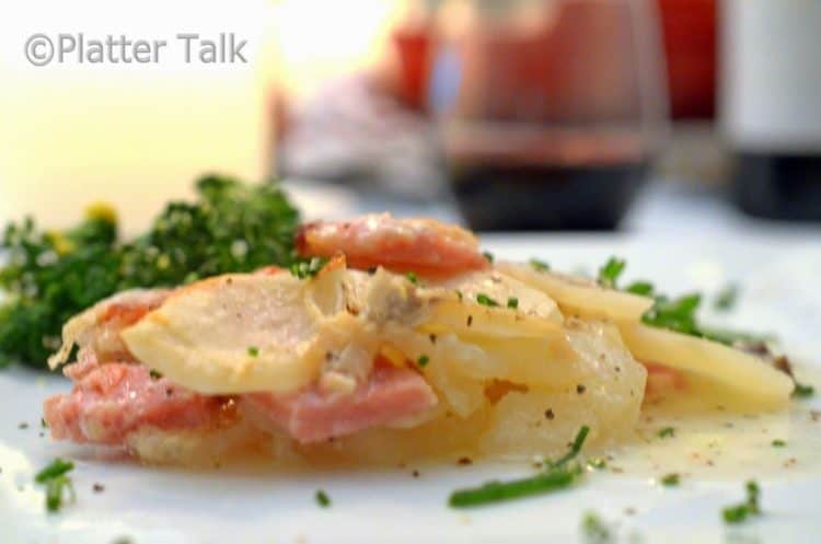 A close up of a plate of scalloped potatoes and ham