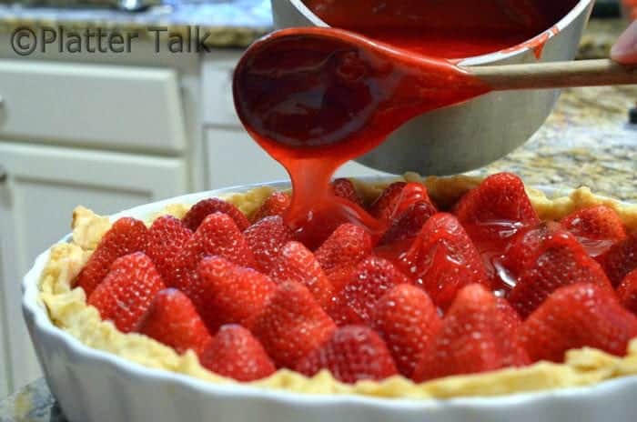 strawberry sauce getting poured over a strawberry pie