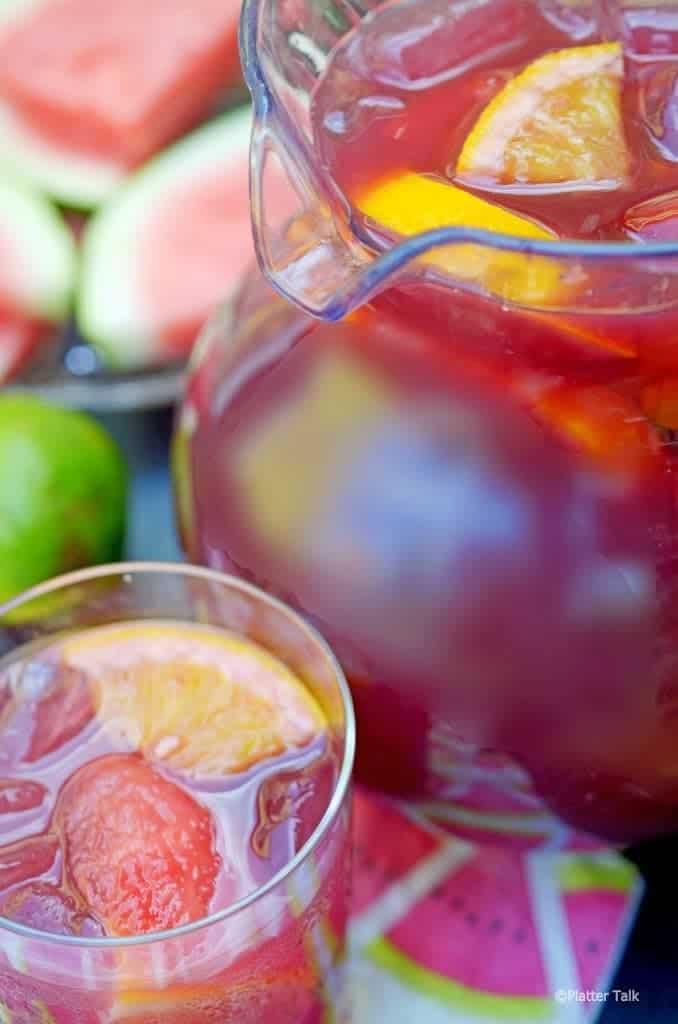 Pitcher of homemade sangria with vodka and glass and tray of watermellon.