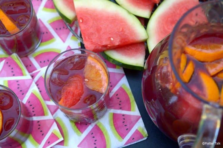 Three glass of red wine vodka sangria with full pitcher, garnished with mellon.