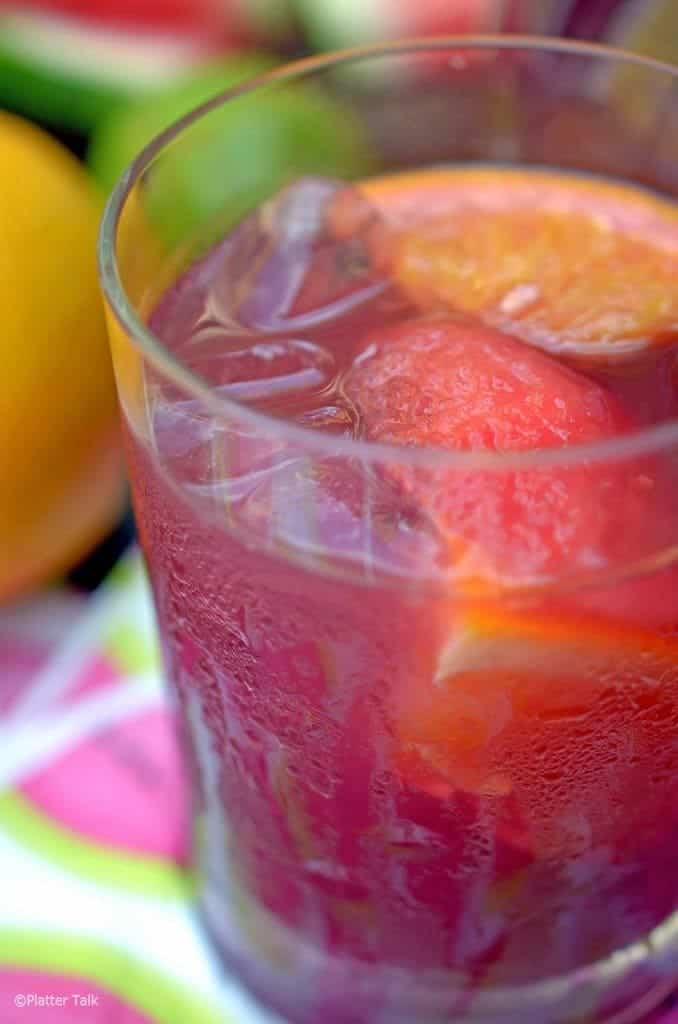 Glass of red sangria with peach and orange slices.