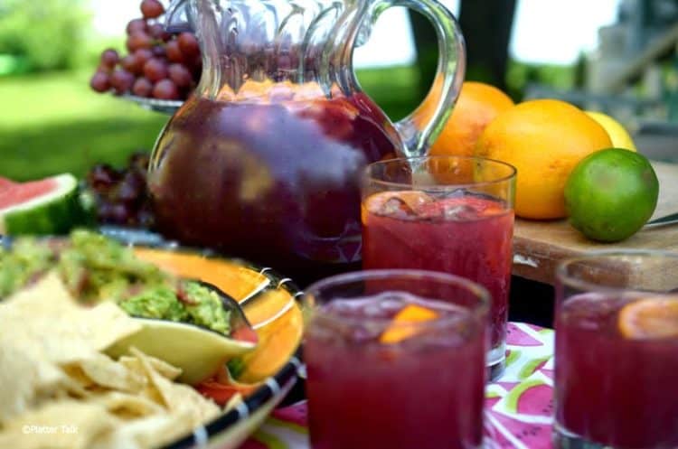 Outdoor table of homemade sangria, oranges, grapes and a bowl of guacamole.