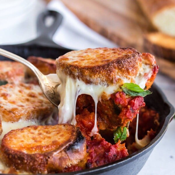 Scooping a portion of meatballs and bread out of skillet with melted cheese.