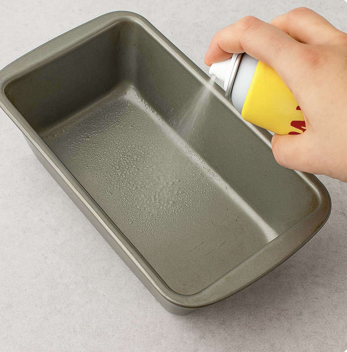 Spraying a loaf pan with non-stick spray.