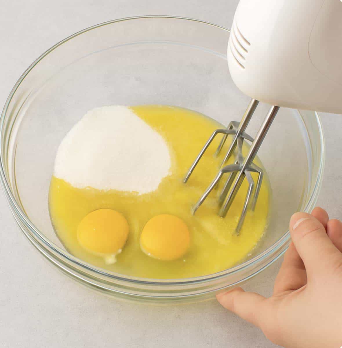 Beating some eggs and sugar in a mixing bowl.