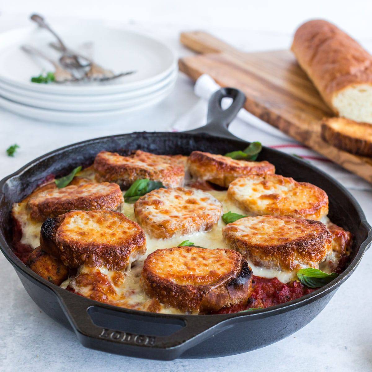 Skillet with sliced baguettes and melted cheese in red sauce.