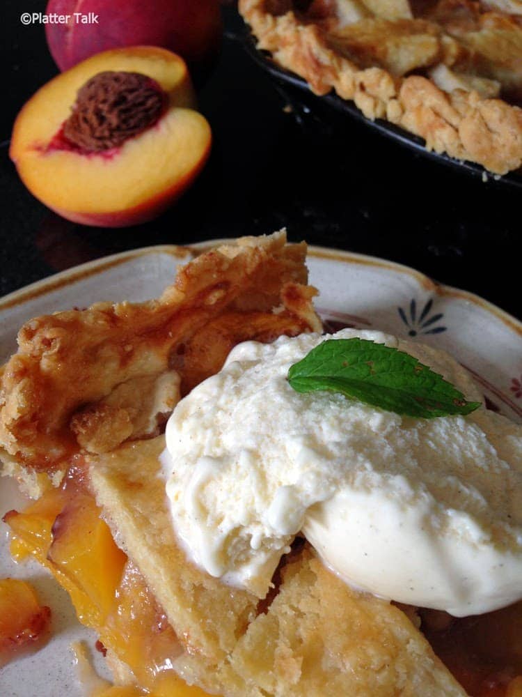 A slice of peach pie with ice cream on a plate.