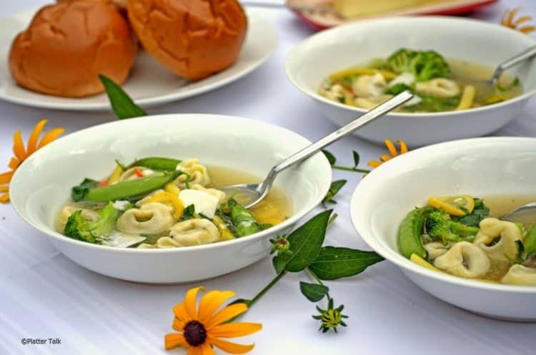 A bowl of soup on a table, with Tortellini.