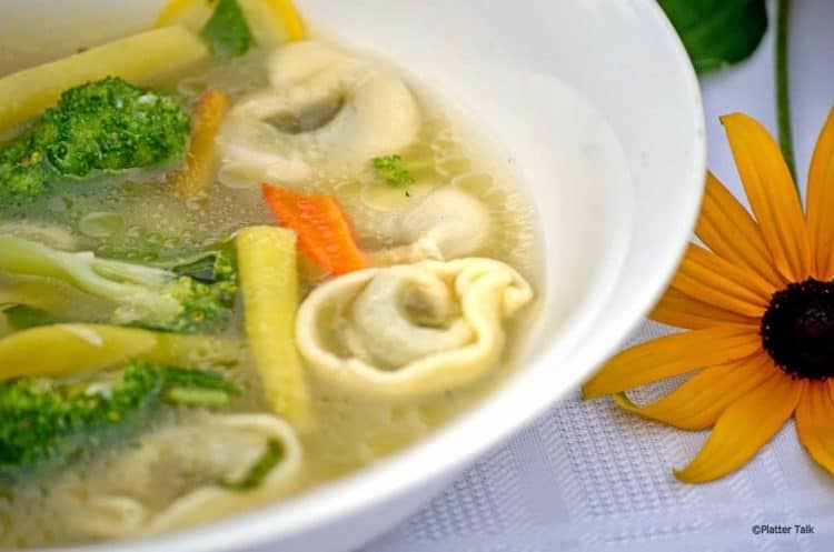 A bowl of soup with broccoli and tortellini. 