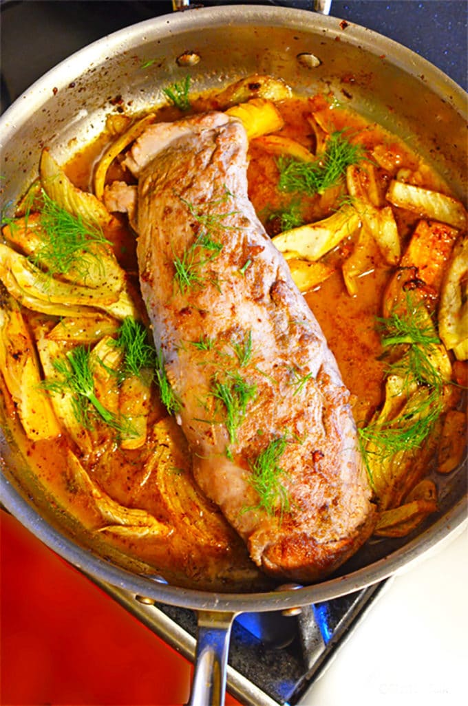 Pork tenderloin in a skillet with fronds of fennel.